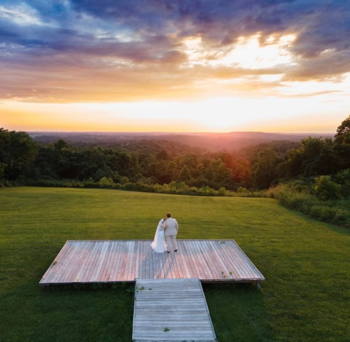 A couple standing on a platform overlooking a sunset at Burdoc Farms